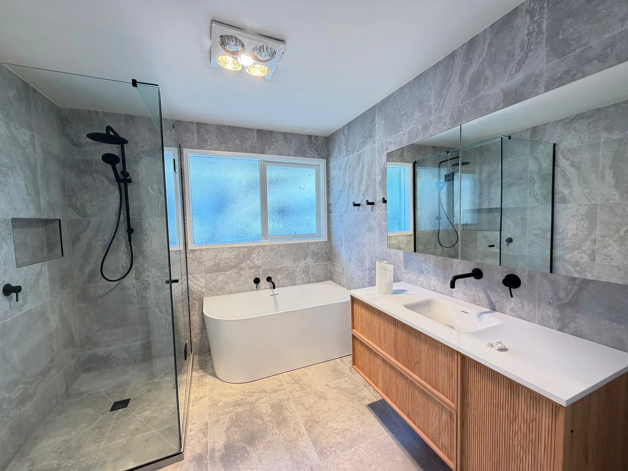 Completed bathroom with a freestanding bath, timber vanity and grey tiles